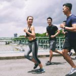 Young cheerful people running behind pretty fit woman
